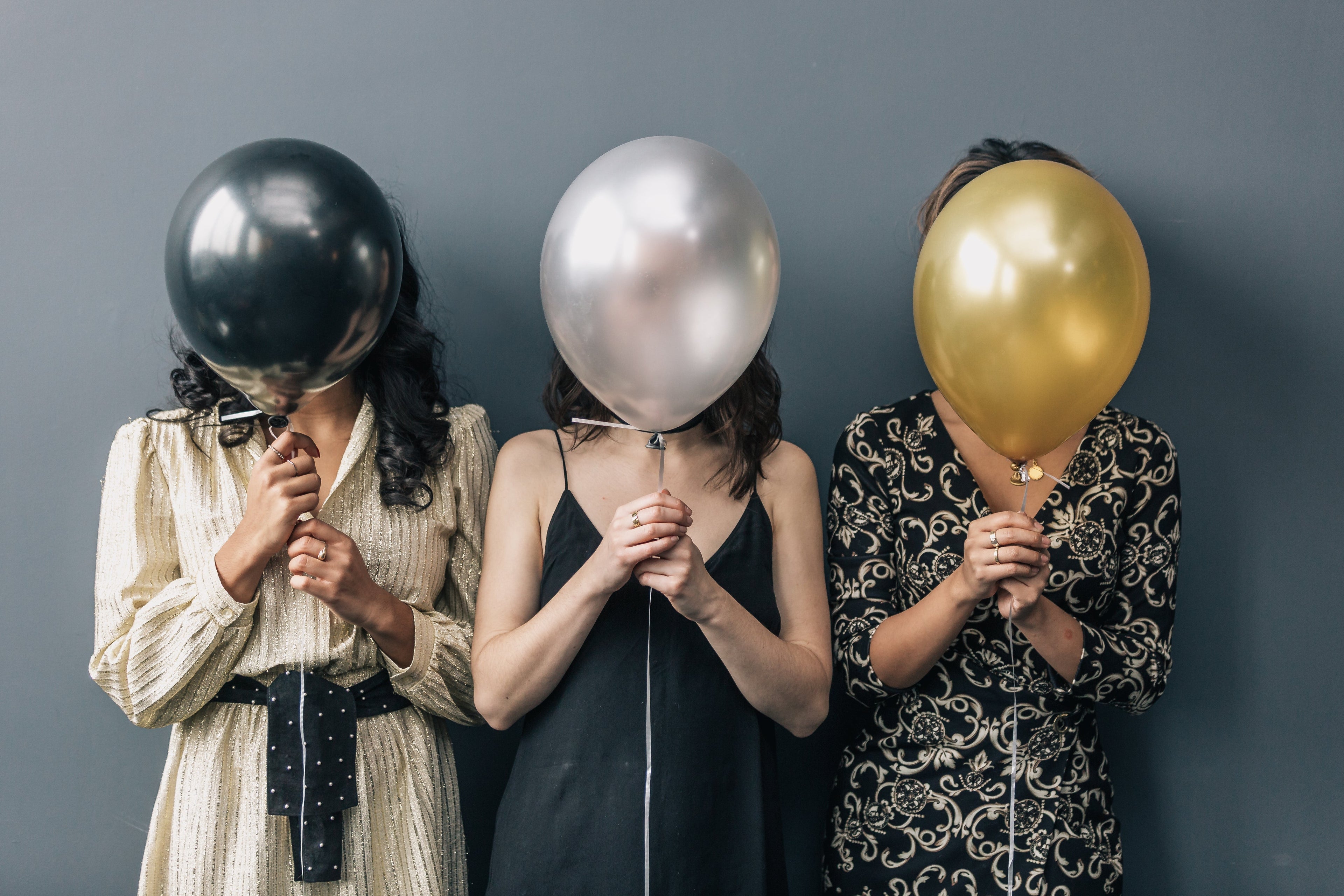 three women with balloons covering their faces