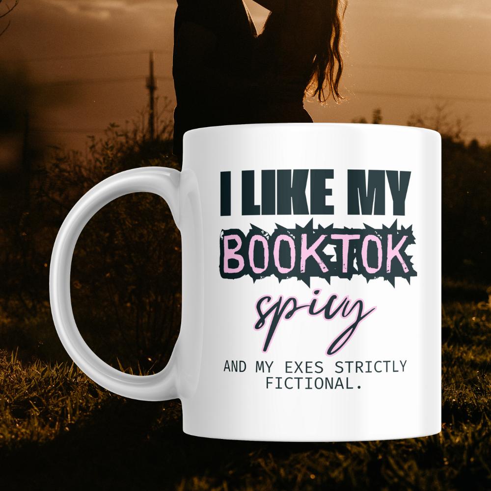 Mug with text 'I like my book-tok spicy and my exes strictly fictional' in front of a sunset silhouette of a couple.