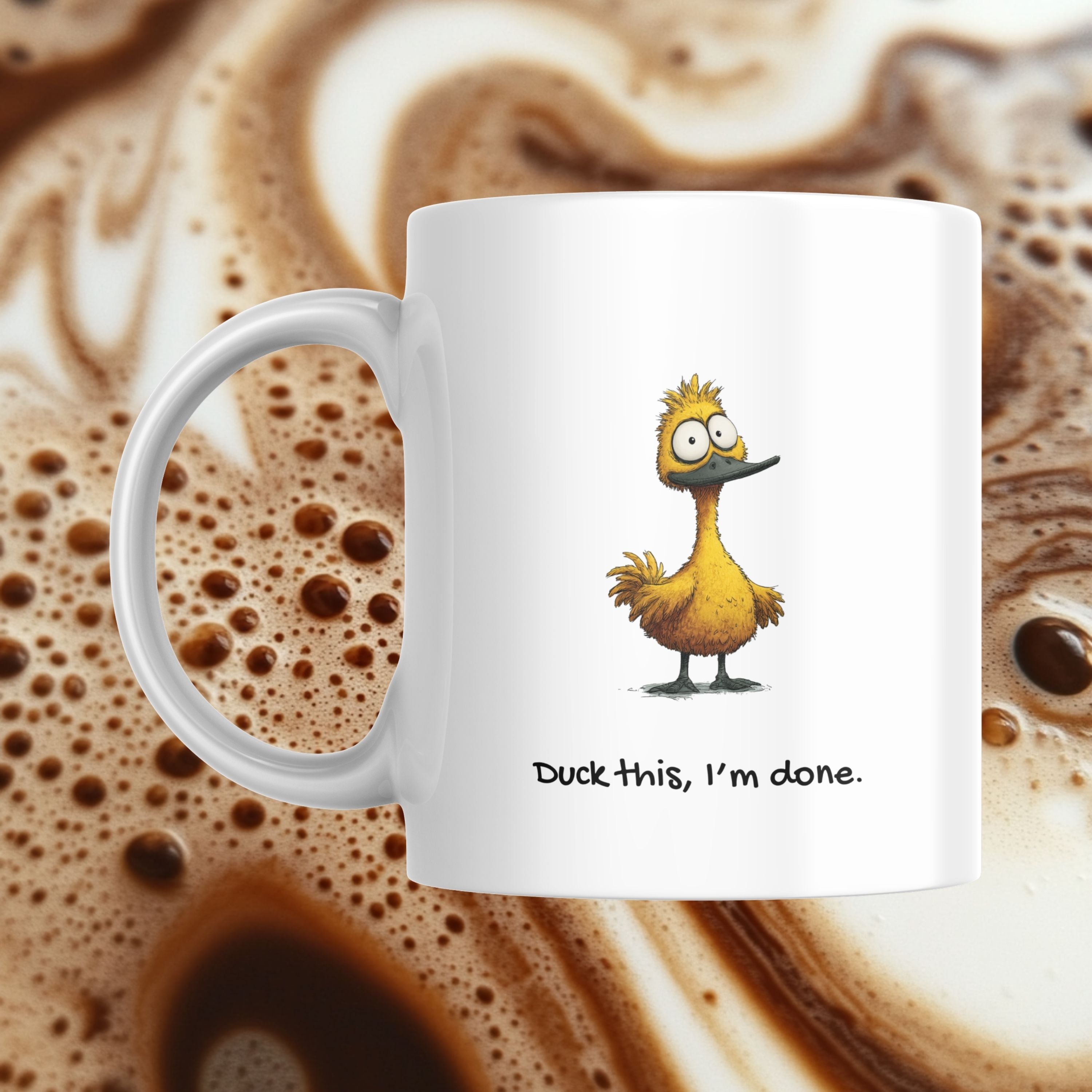 White mug with a cartoon duck design and text 'Duck this, I'm done.' against a background of coffee with foam.