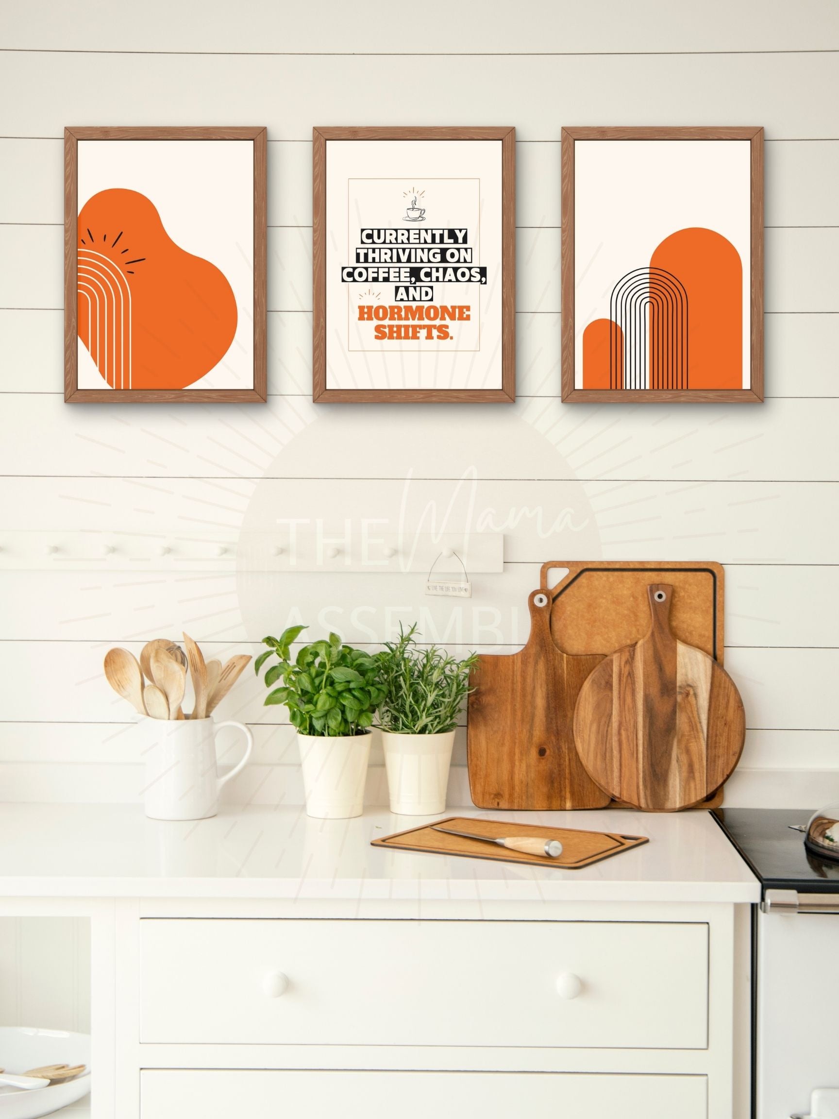 Three framed prints on a wall above a kitchen counter with cutting boards and utensils.
