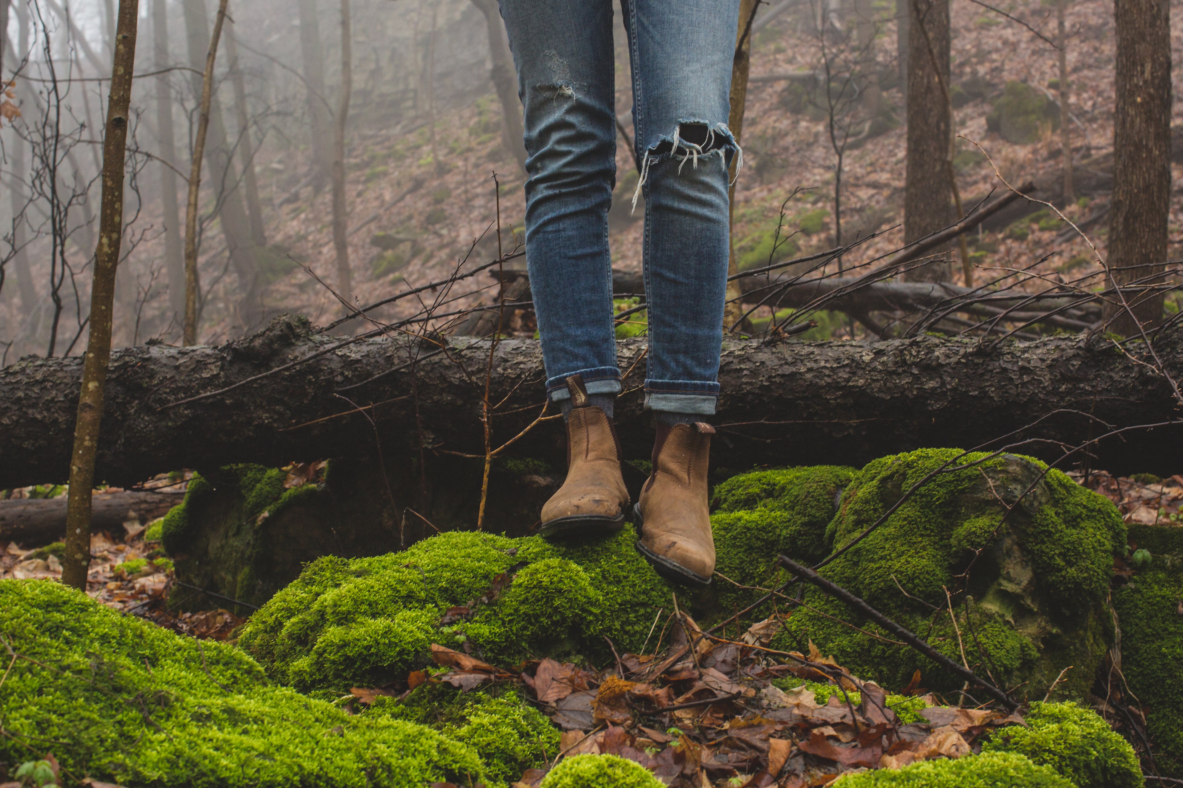 brown pair of boots and ripped jeans image of a woman standing in a forest