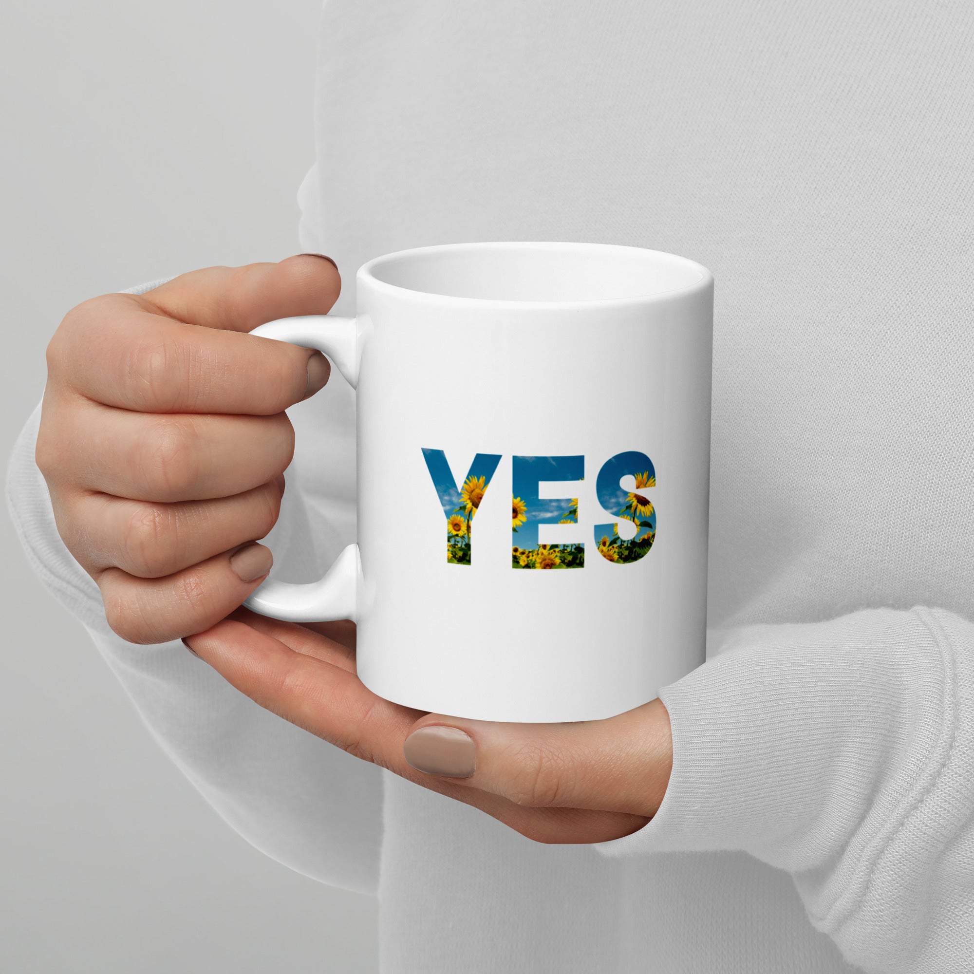 White mug with 'YES' printed on it held by a person against a gray background