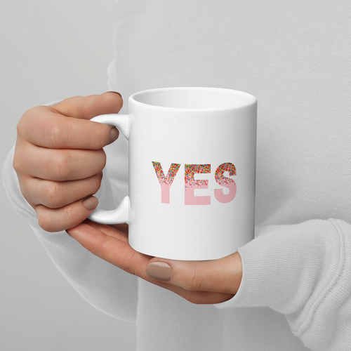 White mug with 'YES' printed on it held by a person against a gray background