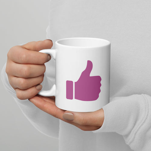 White mug with a pink thumbs-up icon held by a hand against a gray background