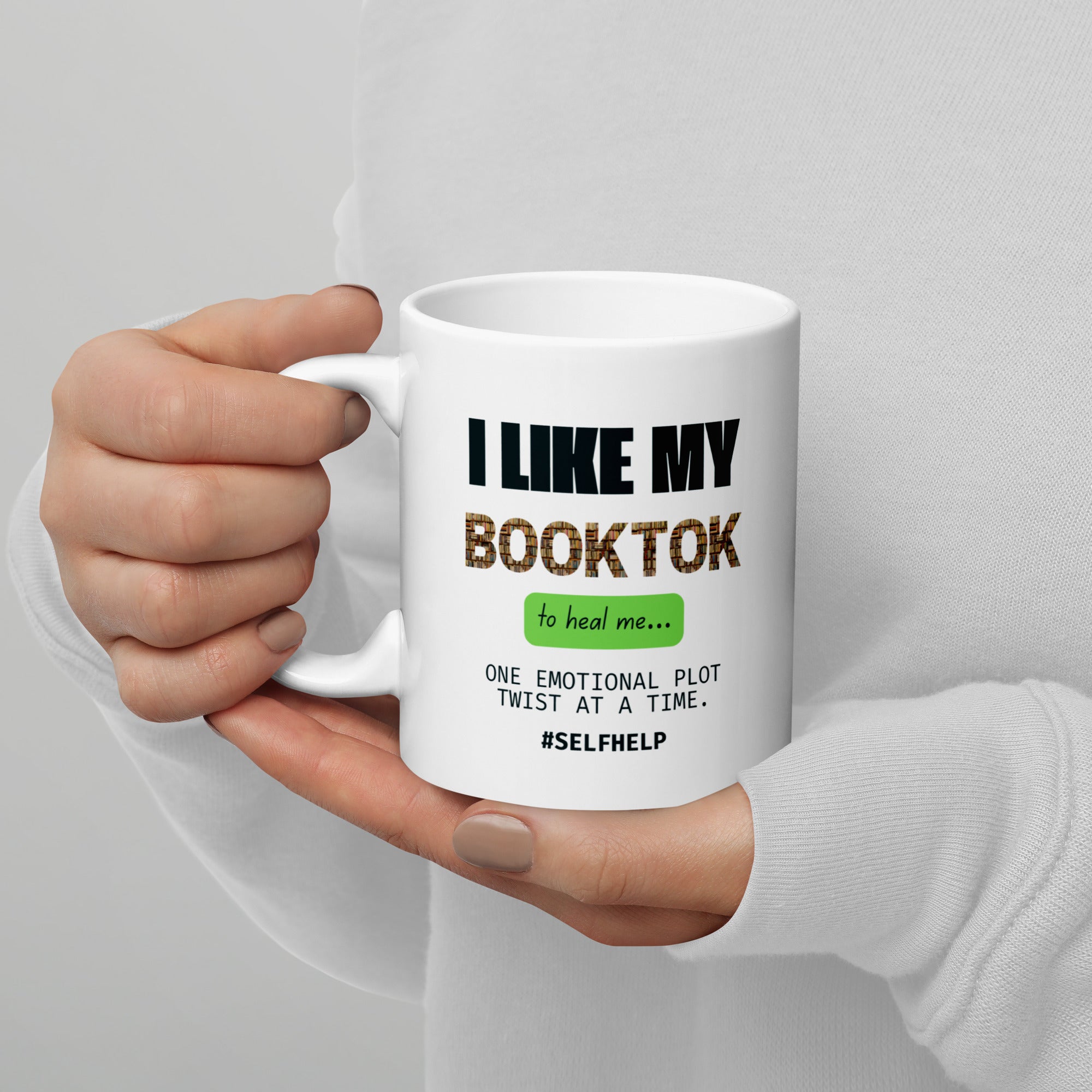 White mug with text held by a hand against a gray background