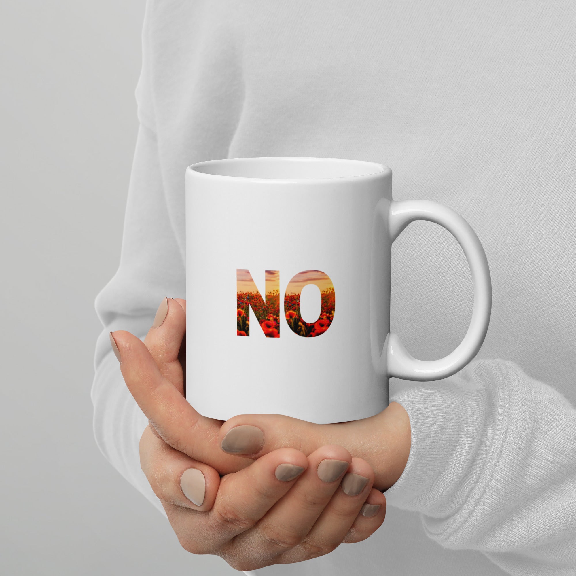 White mug with 'NO' printed on it held by a person against a gray background