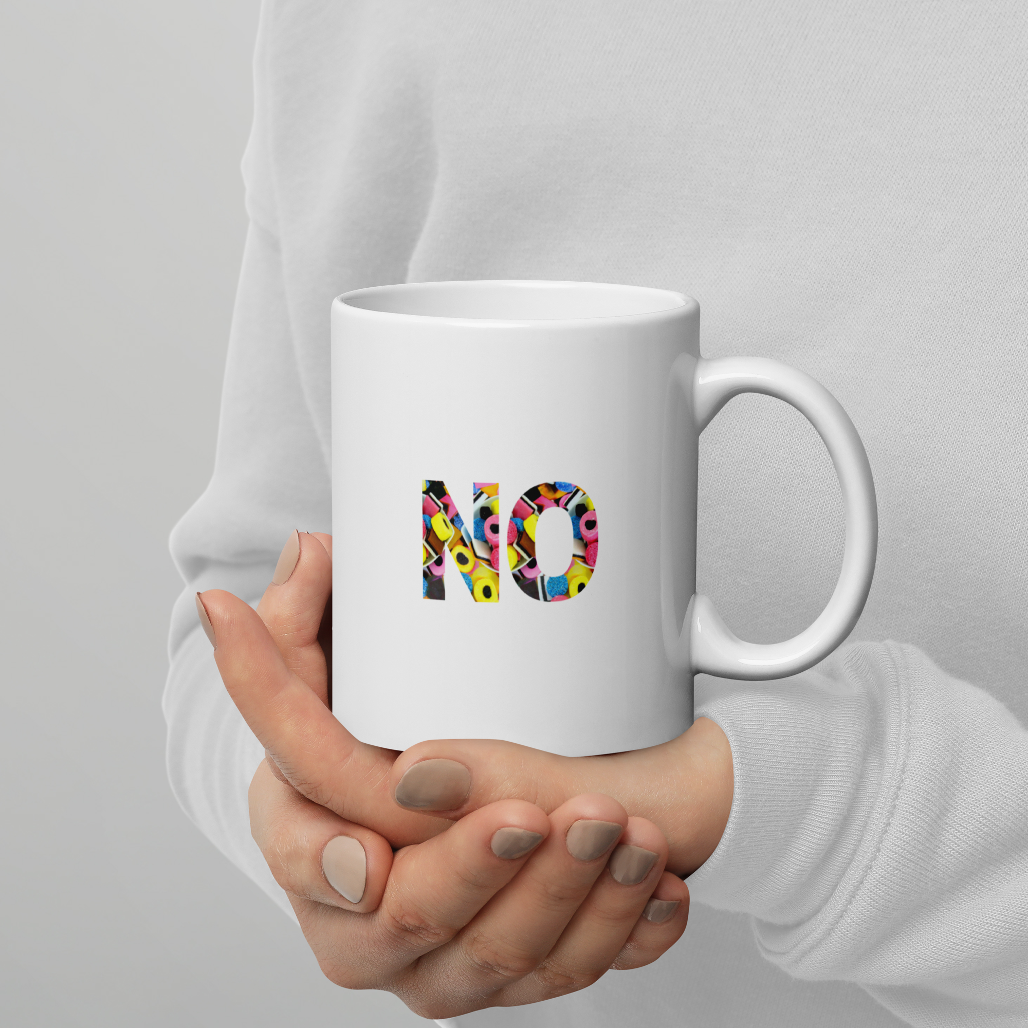 Hand holding a white mug with colorful letters spelling 'NO' on a plain background