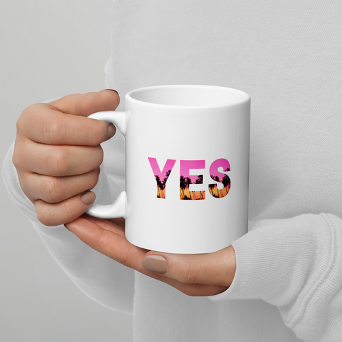 White mug with 'YES' printed on it held by a person against a gray background